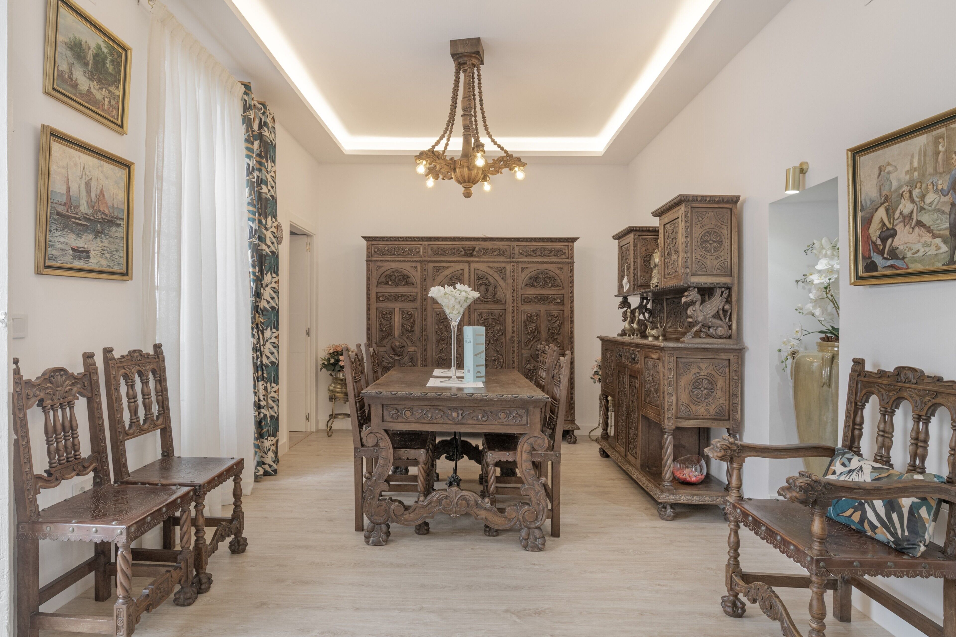 Una habitación con una mesa de madera, sillas, una araña y armarios de madera decorados.