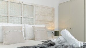 Une chambre à coucher avec un lit, des oreillers, une couverture, une armoire et une fenêtre avec un luminaire.
