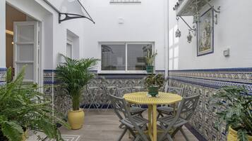 Un patio con una mesa redonda y sillas, macetas con plantas y una pared con diseño geométrico de azulejos.