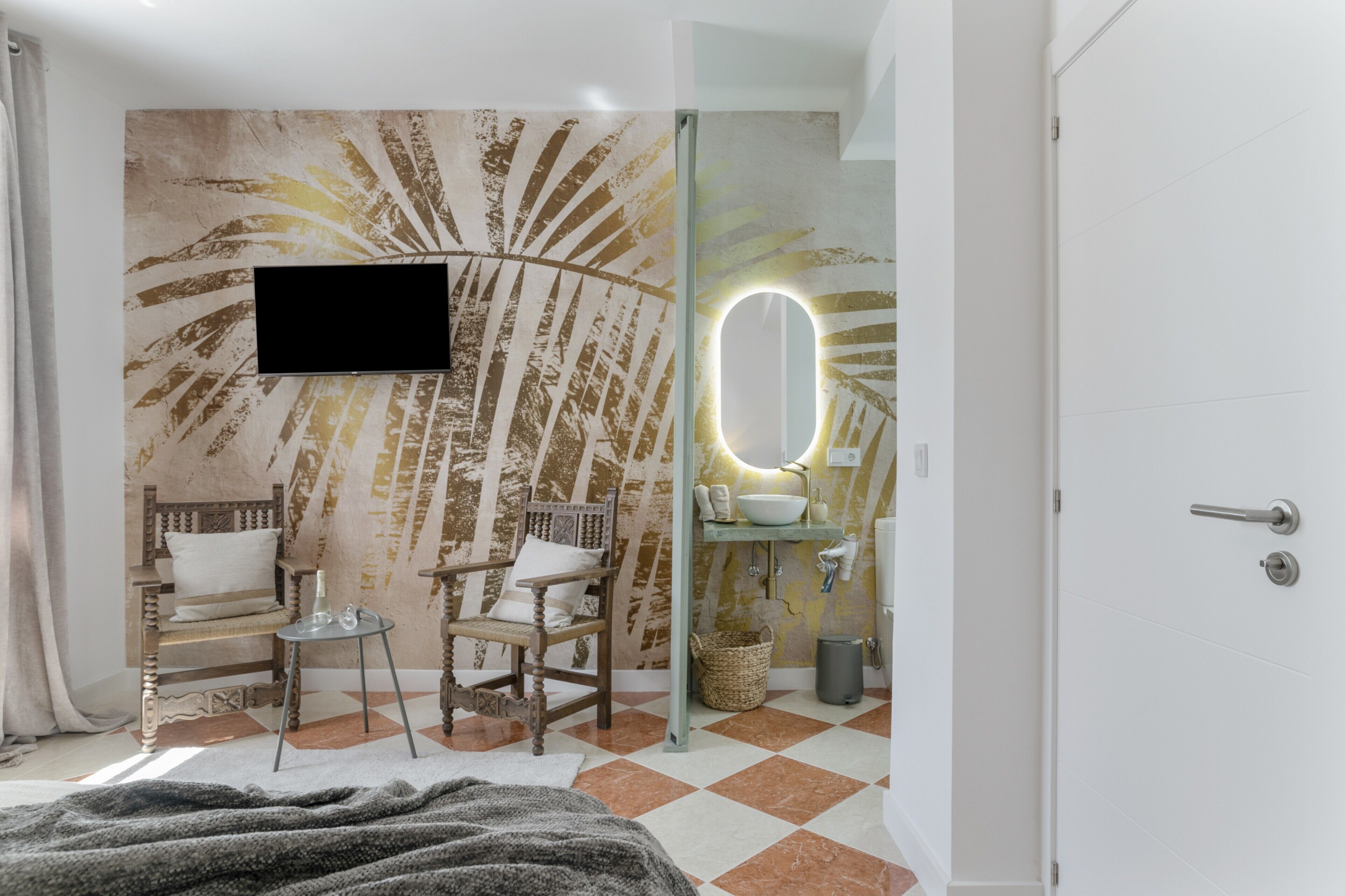 Un baño con un espejo grande, un lavamanos, un televisor montado en la pared y una silla.