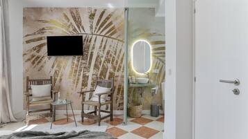 Un baño con un espejo grande, un lavamanos, un televisor montado en la pared y una silla.