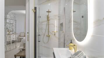 Une salle de bain moderne avec une douche à parois de verre, un lavabo blanc doté de robinetterie dorée et un grand miroir.