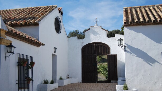 A courtyard with a cobblestone path, a large wooden gate, and white buildings with tiled roofs. - Villa 'La Priorita' with Mountain View, Wi-Fi and Air Conditioning (Córdoba)
