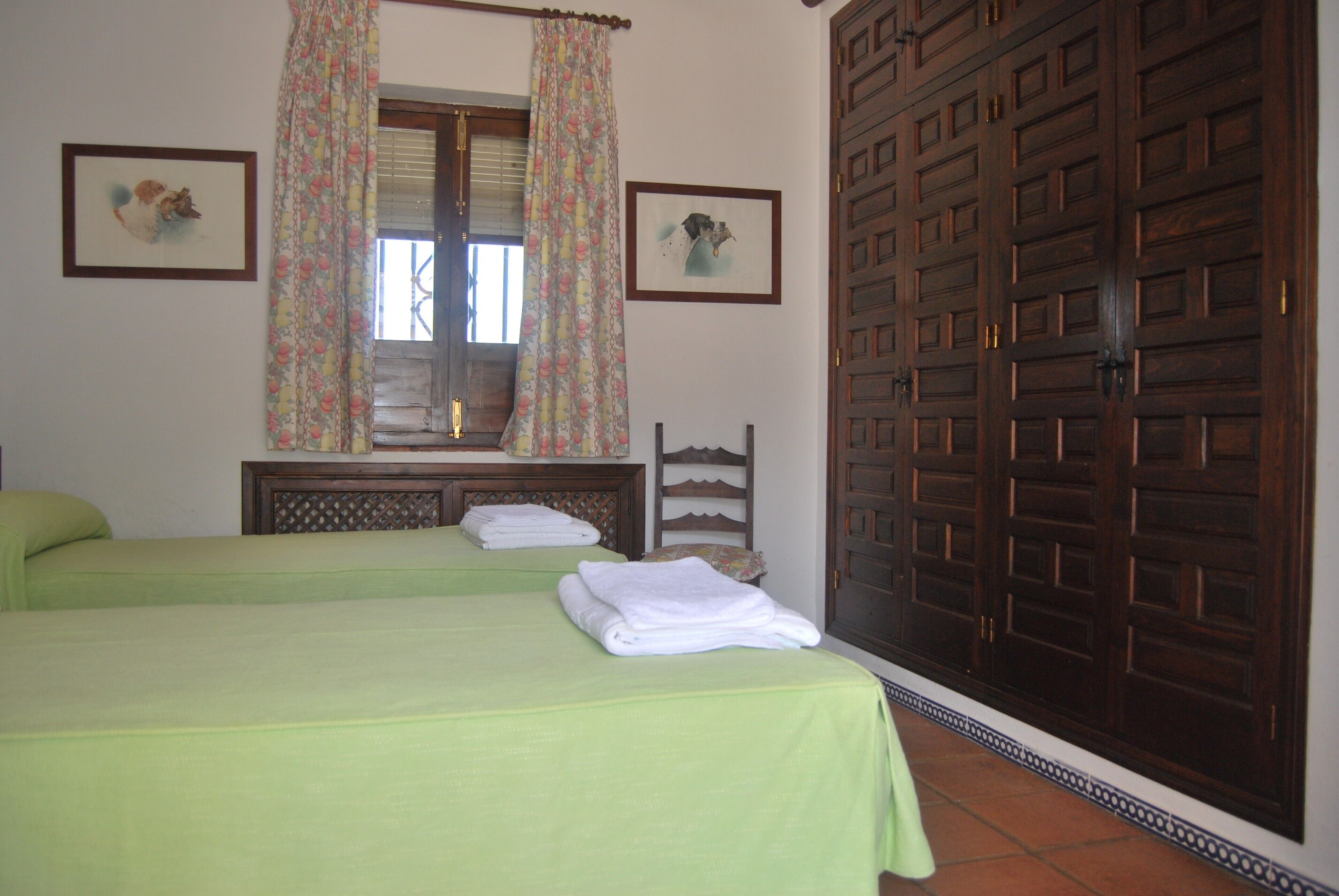 Une chambre avec deux lits, une armoire en bois et deux tableaux encadrés accrochés au mur.