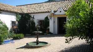 A courtyard with a fountain, a tiled roof, and a white building with a door. - Villa 'La Priorita' with Mountain View, Wi-Fi and Air Conditioning (Córdoba)