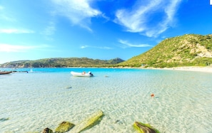 A clear coastal beach with a boat, rocky shoreline, and hills in the background. - Apartment 'La Casetta Di Lulu' with Private Terrace, Private Garden and Air Conditioning (Villasimius)