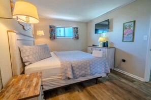 A bedroom with a bed, bedside table, lamp, TV, and artwork. - Meridian 307 (Myrtle Beach)