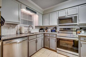 Una cocina con armarios blancos, un microondas de acero inoxidable y un horno doble.