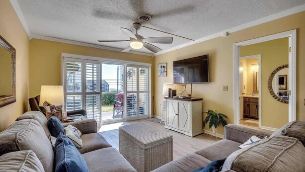 A living room with a ceiling fan, a TV, a sofa, a cabinet, and a sliding glass door leading to an outdoor area.