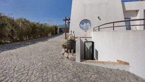 A modern building with a stone-paved pathway leading to a wooden door, surrounded by vegetation.