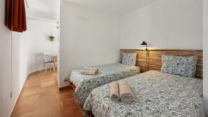 A bedroom with two beds, a wooden headboard, a bedside lamp, and a small desk with a chair.