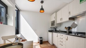 A kitchen with white cabinets, a black countertop, a hanging light fixture, and a trash bin.