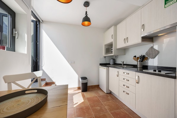 A kitchen with white cabinets, a black countertop, a hanging light fixture, and a trash bin.