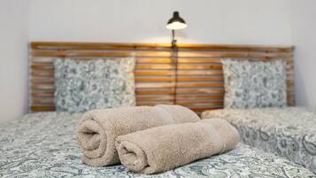 A bed with rolled towels, a wooden headboard, patterned bedding, and a bedside lamp.