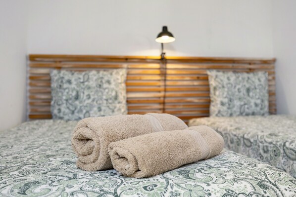 A bed with rolled towels, a wooden headboard, patterned bedding, and a bedside lamp.