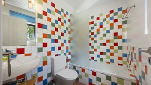 A bathroom with a white sink, toilet, and bathtub, tiled with multicolored square tiles.