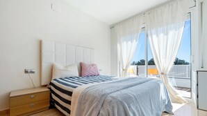 A bedroom with a bed, a nightstand, a window with curtains, and a view of the outside.