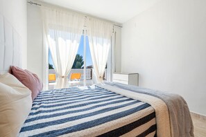 Ett sovrum med en säng, gardiner, utsikt över omgivningen och ett litet bord.