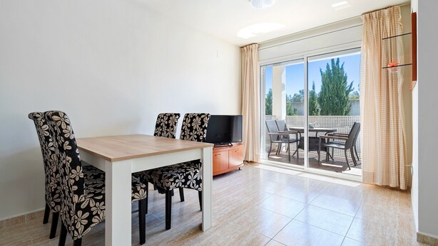 A dining area with a table and chairs, a television, and a sliding glass door leading to an outdoor patio.