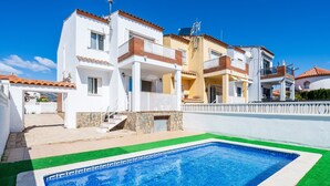A swimming pool with a clear blue water edge, surrounded by a white building with balconies and a stone wall.