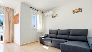 A modern living room with a grey sofa, a window with curtains, an air conditioner, and a painting on the wall.