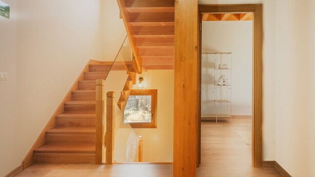 A wooden staircase leading to a second floor, a small window with a view, and a wooden door frame.