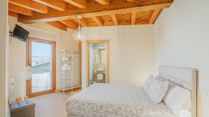 A bedroom with a bed, a bedside table, a nightstand, a wardrobe, a mirror, and a door leading to a balcony.