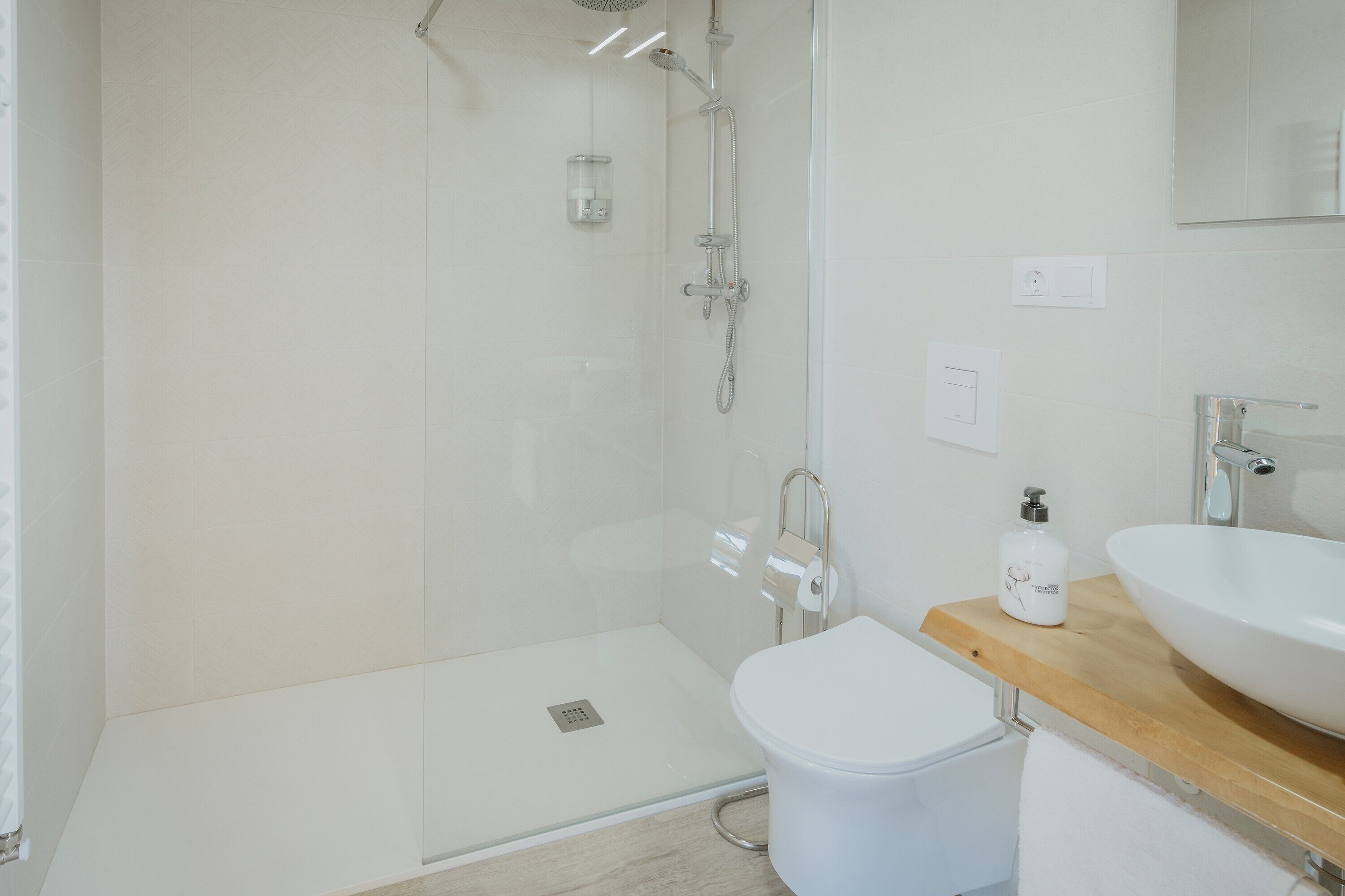 A modern bathroom with a glass-enclosed shower, a white toilet, and a wooden vanity with a large sink.