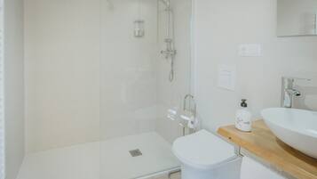 A modern bathroom with a glass-enclosed shower, a white toilet, and a wooden vanity with a large sink.