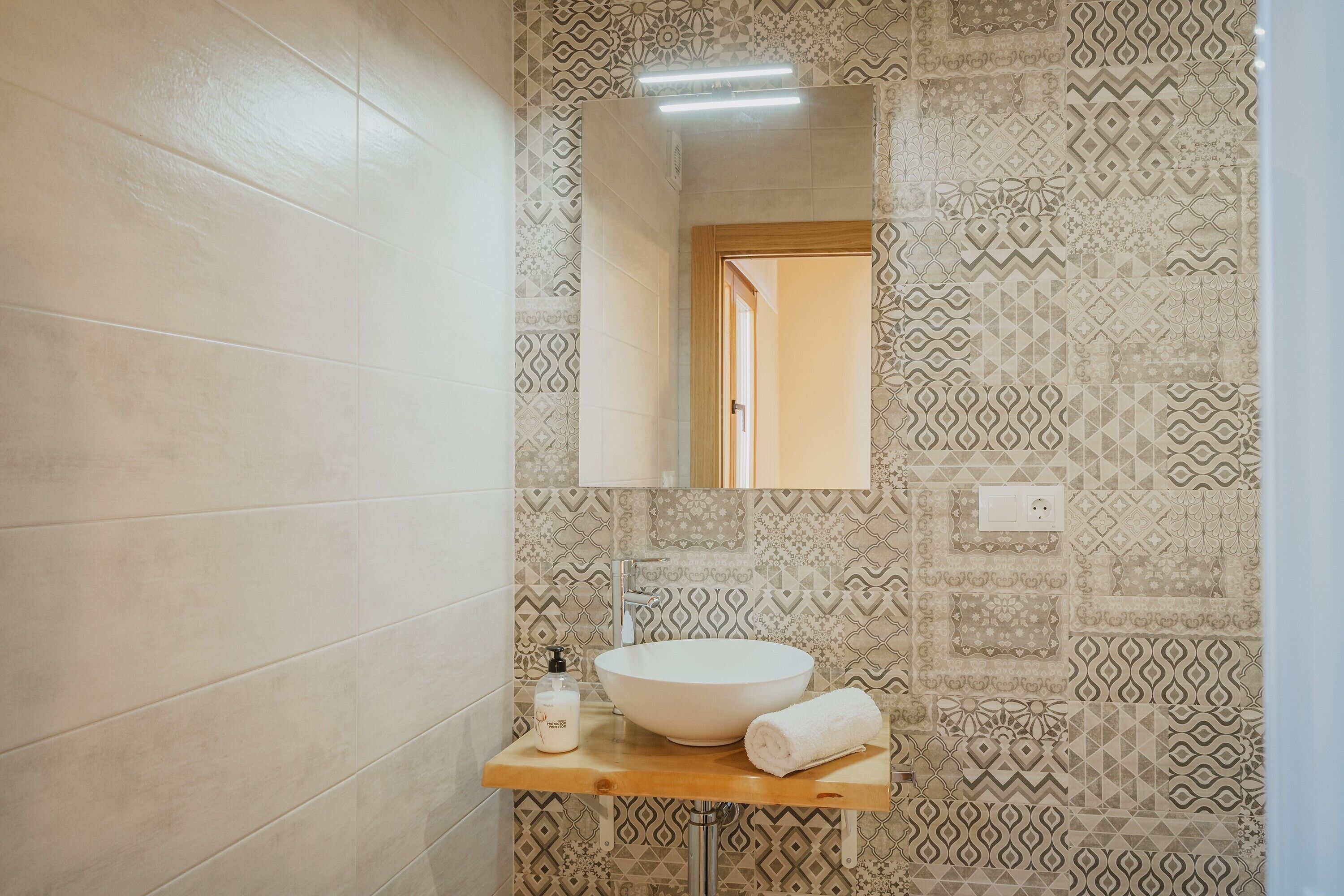 A bathroom with patterned tiles, a wooden vanity, a white sink, a towel, and a mirror.
