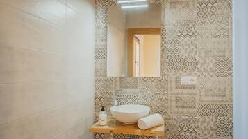 A bathroom with patterned tiles, a wooden vanity, a white sink, a towel, and a mirror.