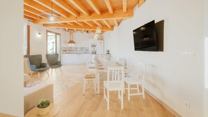 A spacious living area with a dining table, chairs, and a TV mounted on the wall.