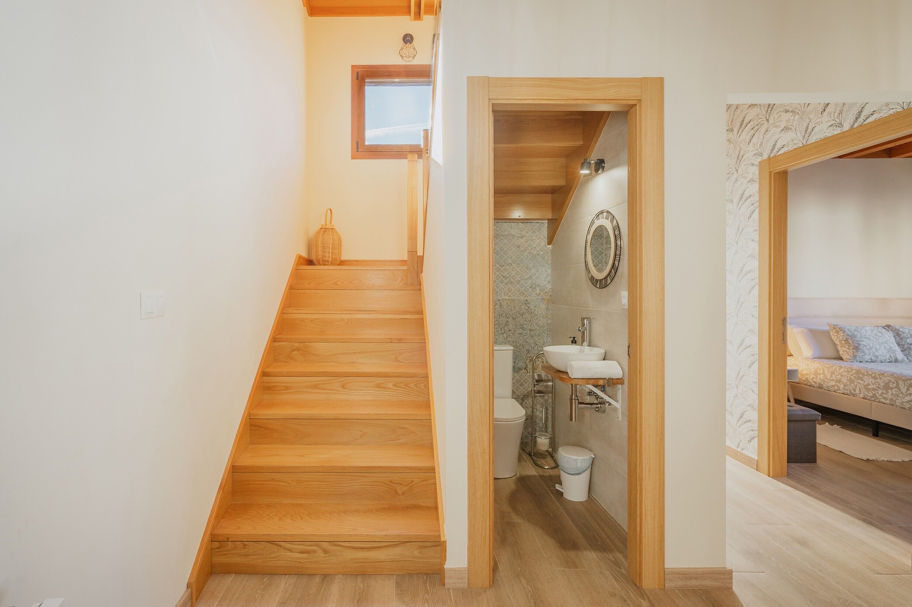 Una scala in legno conduce a un bagno con il water, un lavandino e uno specchio.