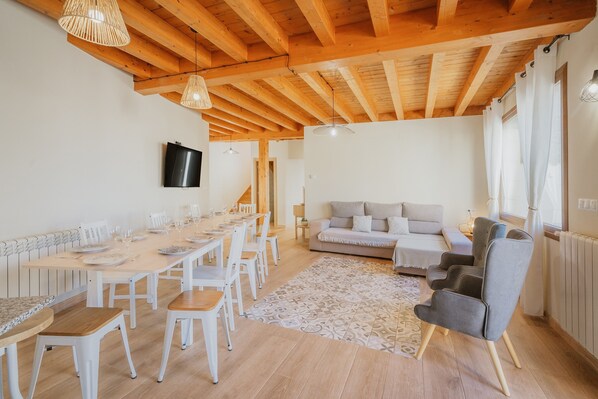 Un comedor con una mesa larga y sillas, un sofá y un televisor en la pared.