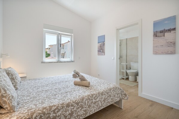 A bedroom with a bed, a window, a bathroom, and a door.