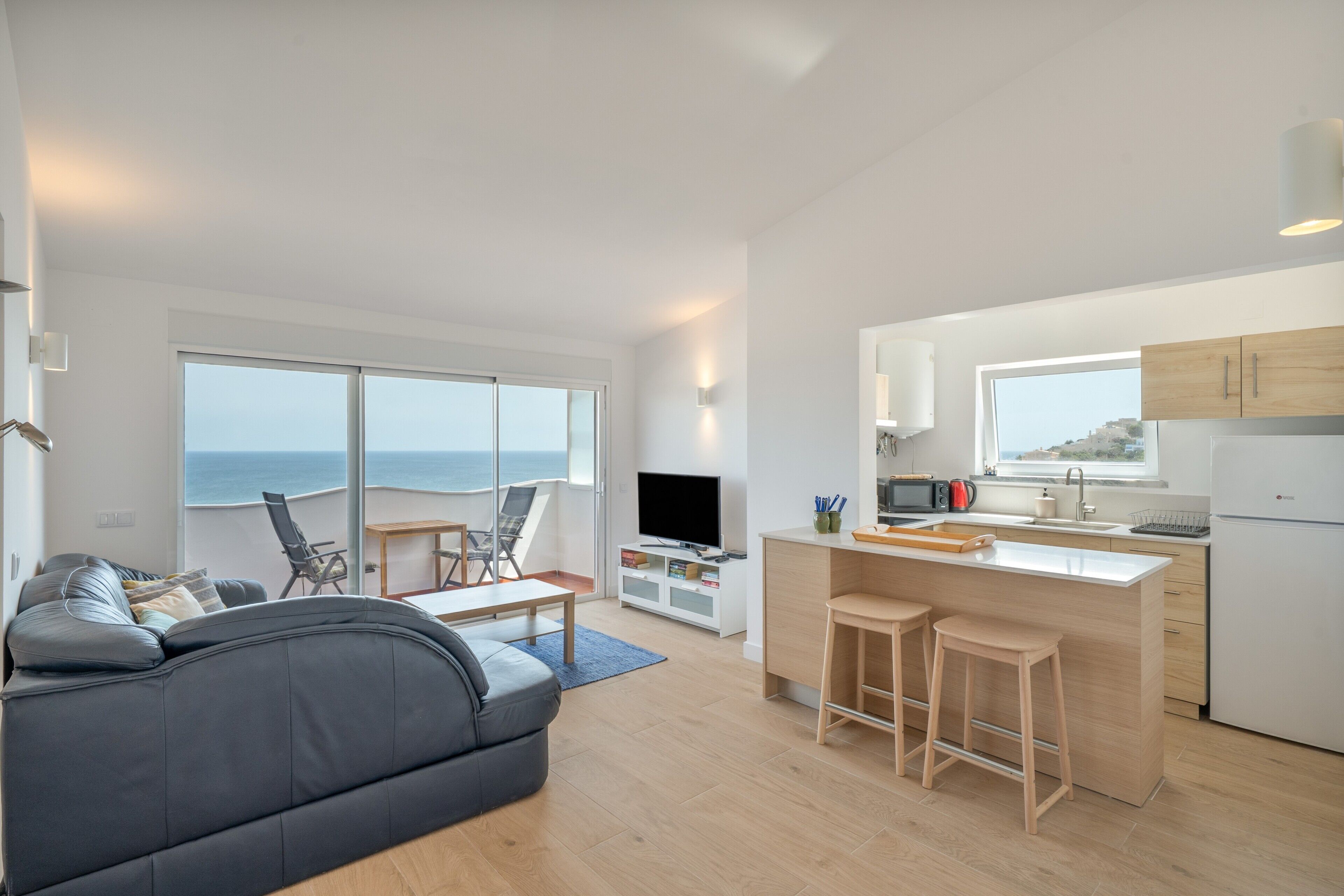 Un salón moderno con un sofá, un televisor y un balcón con vistas al mar.