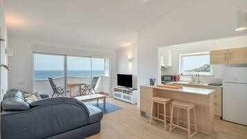 Un salón moderno con un sofá, un televisor y un balcón con vistas al mar.