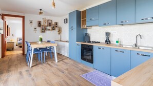 Een moderne keuken met blauwe kastjes, een houten eettafel en een zichtbare oven.