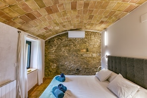 Une pièce avec un mur en pierre, un lit recouvert de draps blancs et une fenêtre avec des rideaux.