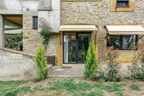 Un bâtiment en pierre avec une porte d’entrée en verre, une plaque portant l’inscription « ALZINA », et une petite marche menant à la porte.