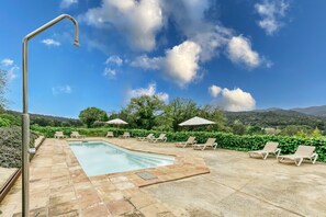Piscina com espreguiçadeiras e guarda-sóis, rodeada por vegetação e colinas.