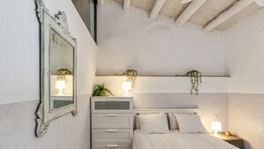 A bedroom with a bed, a dresser, a mirror, and a nightstand with a lamp.
