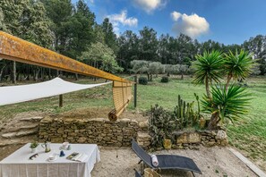 Un tavolo apparecchiato all'aperto con tovaglia bianca, un muro in pietra e un'amaca.
