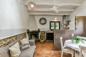 Uma sala de estar acolhedora com um sofá, lareira, mesa de jantar para dois e cozinha ao fundo.