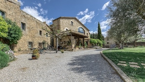 A stone building with a covered patio, gravel driveway, and surrounding greenery. - Country House 'Casa Rural La Pallissa Con Piscina' with Mountain View, Shared Pool and Wi-Fi (Llampaies)