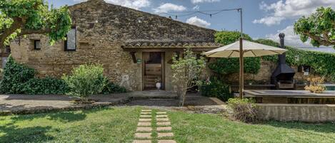 Un edificio de piedra con tejado de tejas, entrada pavimentada y jardín con camino de piedra.