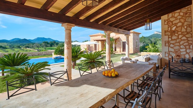 A wooden table with a bowl of fruit, outdoor seating, a pool, and a view of mountains. - Country House 'Sant Salvador' with Mountain View, Wi-Fi and Air Conditioning (Illes Balears)