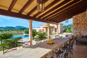 Une table en bois avec un saladier de fruits, des sièges d’extérieur, une piscine et une vue sur les montagnes.