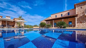 A swimming pool with tiled flooring, a lounge area with chairs, and a building with stone walls and a tiled roof. - Country House 'Sant Salvador' with Mountain View, Wi-Fi and Air Conditioning (Illes Balears)