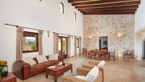 A spacious living area with a sofa, wicker chairs, a coffee table, and a stone wall. - Country House 'Sant Salvador' with Mountain View, Wi-Fi and Air Conditioning (Illes Balears)